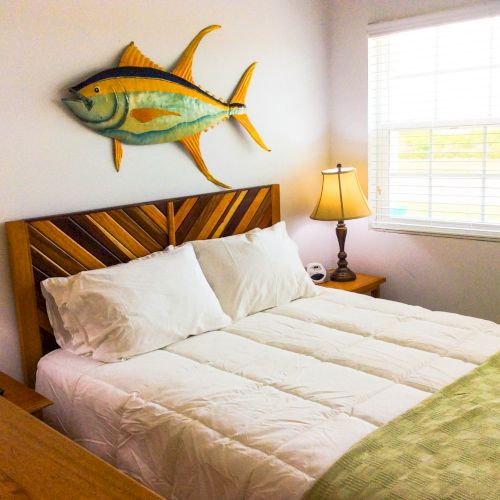 A cozy bedroom with a wooden bed, bedside lamps, and a large fish wall d&eacute;cor above the headboard, next to a sunny window.