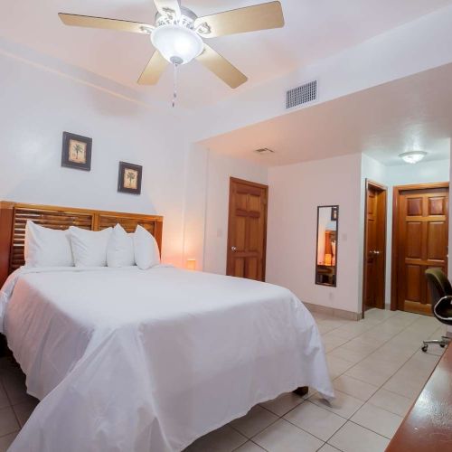 A tidy hotel bedroom with a king bed, ceiling fan, nightstands, tiled floor, and wooden doors.